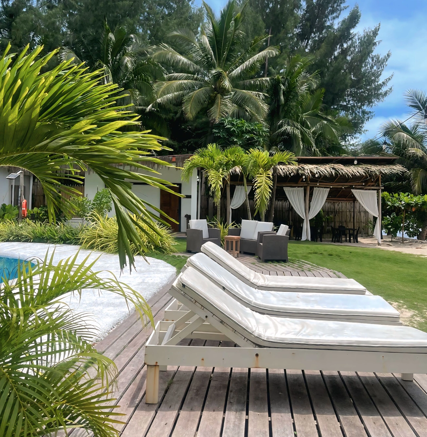 Lush tropical resort with lounge chairs by pool and thatched-roof cabana