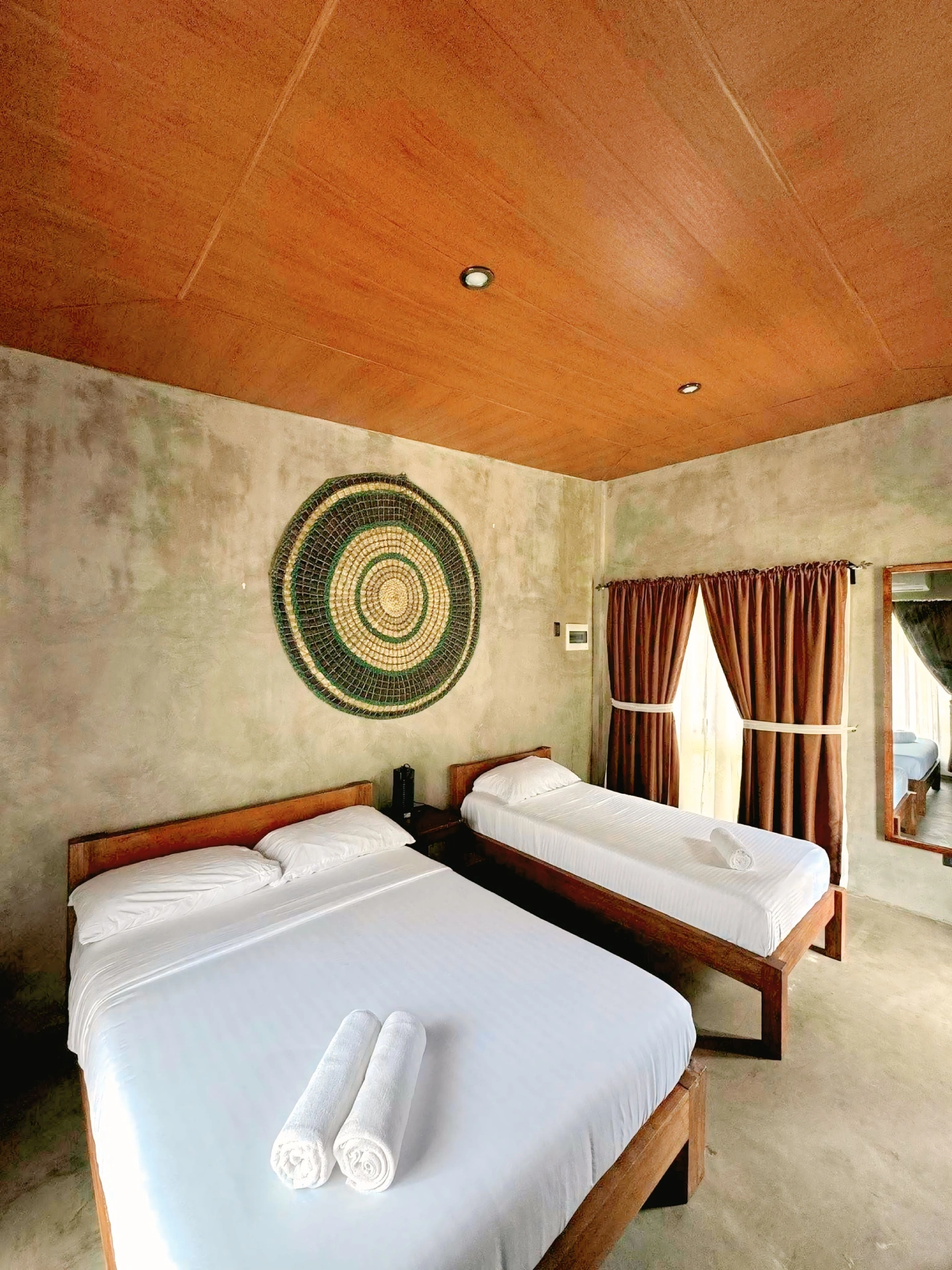 Interior of a hotel room with two beds, rustic decor, and wooden ceiling.