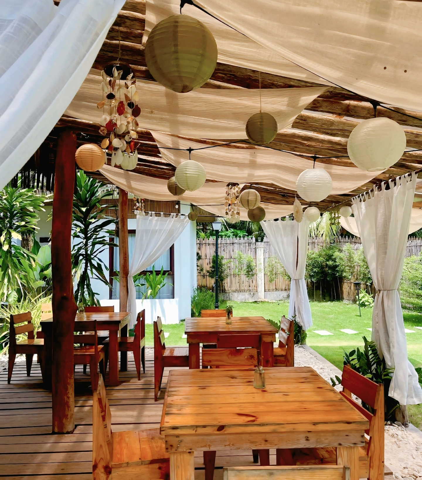 Tropical outdoor dining area with wooden tables and chairs under a canopy.