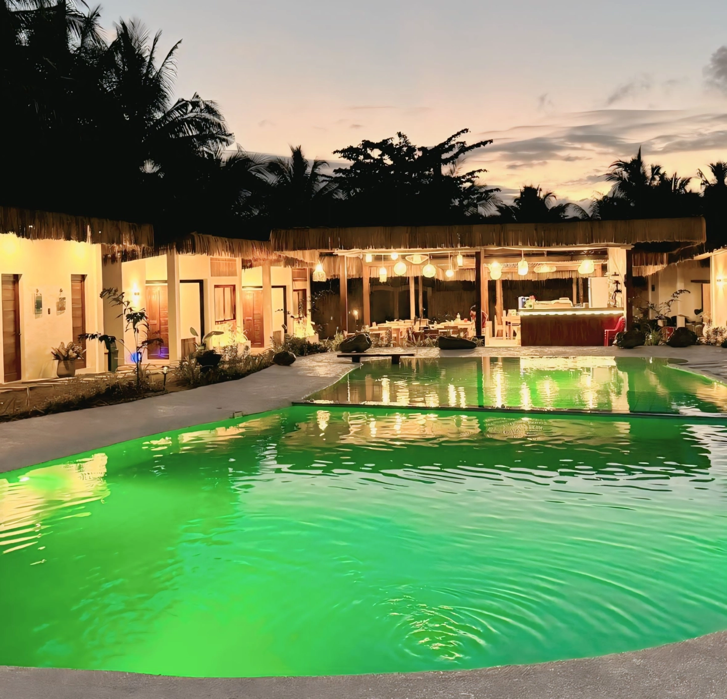 Sun and Waves Resort at dusk, with a brightly lit green pool.