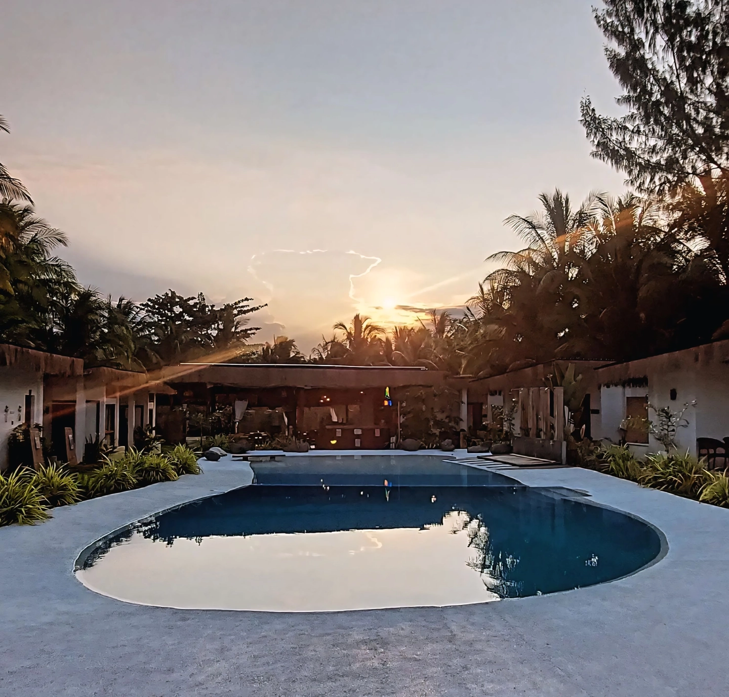 Sunset over the pool at Sun and Waves Resort, surrounded by coconut trees.